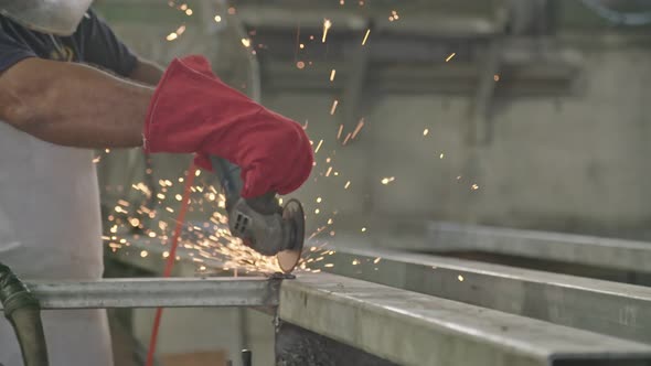 Slow motion of a worker using metal grinder with sparks flying at a metal shop