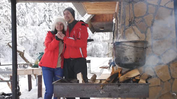 Young Happy Couple on a Winter Day is Prepared in the Courtyard of a Wooden Forest House on an Open