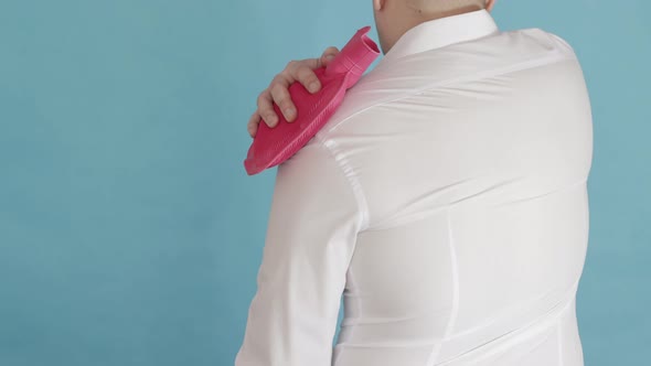 A Male Office Worker Adjusts a Red Heating Pad with Hot Water for Pain in the Shoulder Joint and