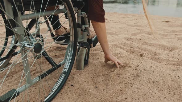 Close Up, Hand of Disabled Person in the Wheelchair Playing with the Sand on the River Coast