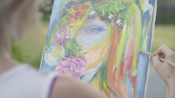 Unrecognizable Woman Painting Summer Woman's Portrait Outdoors. Shooting Over Shoulder of Confident