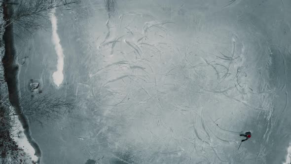 Drone shot flying down towards a single player playing ice hockey on a frozen pond or lake in Canada