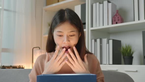 Young Asian woman open the gift box with surprise and sitting on sofa.