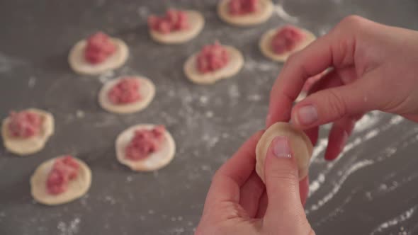 Girl makes homemade ravioli from dough and meat over a gray kitchen table