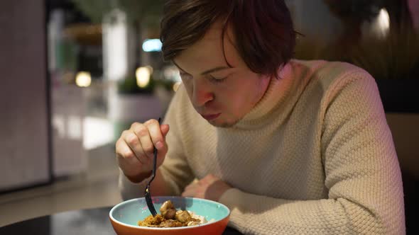 Young Man Enjoys Eating Food for Dinner in Small Cafe