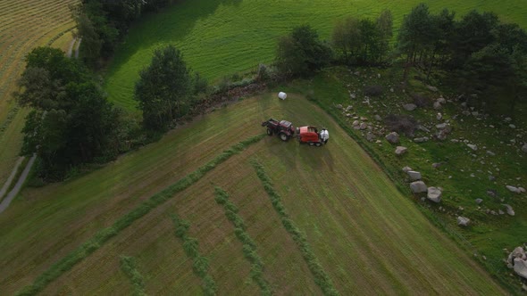 Tractor with baling machine making silage bales on farmland, ascending shot