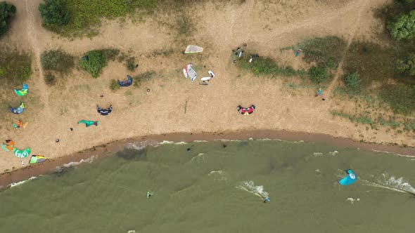 AERIAL: Top View of the Beach Filled With Kite Surfers Preparing to Kite on a Green Colour Sea