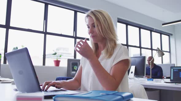 Caucasian businesswoman sitting using laptop in office with coworker in background