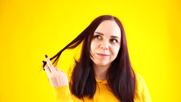 Close Up of Young Woman Twists Her Hair on Yellow Background
