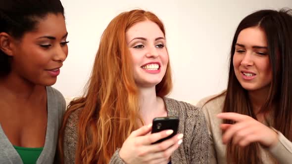 Cute Female Friends Using Smartphone While Sitting On Couch