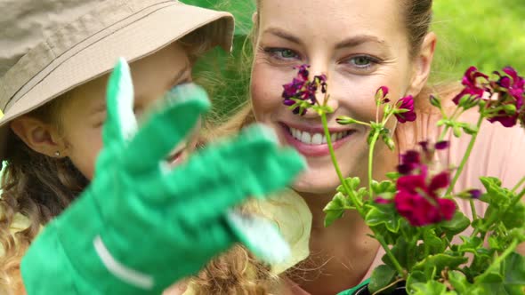 Cute Little Girl Looking At Pot Of Flowers With Her Mother