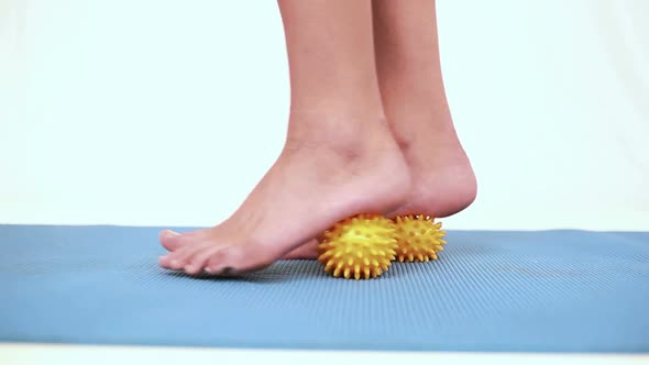 Girl Using Yellow Massage Balls On Her Feet alt