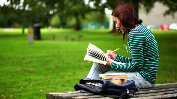 Pretty Student Sitting On Bench Reading A Book Listening To Music