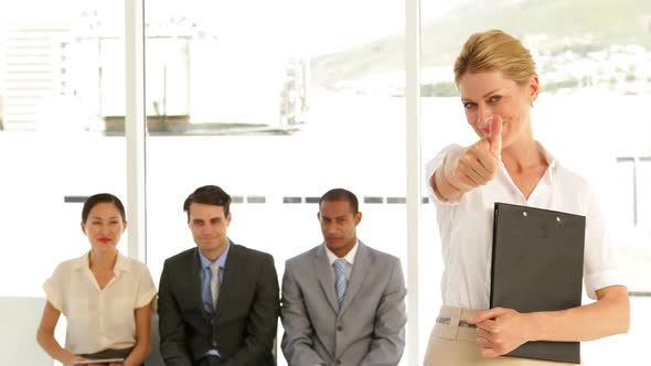 Businesswoman Giving Thumbs To Camera In Front Of Job Applicants