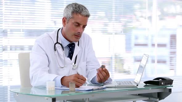 Doctor Looking At Pills While Writing A Prescription