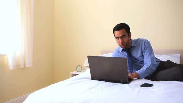 Cheerful Businessman Typing On His Notebook In Bed