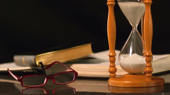 Reading Glasses Falling Beside Hourglass And Bible