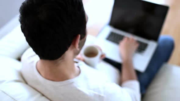 Man Drinking A White Coffee While Using His Laptop