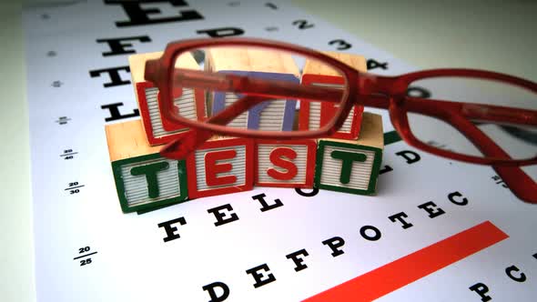 Red Glasses Falling Next To Blocks Spelling Out Eye Test