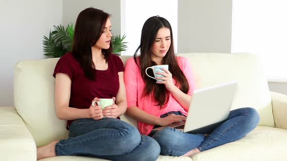 Brunette Using Laptop And Chatting To Her Friend On The Couch Over Coffee