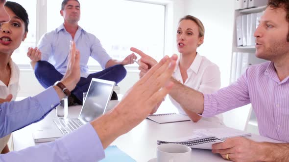 Handsome Businessman Meditating While His Colleagues Are Arguing alt