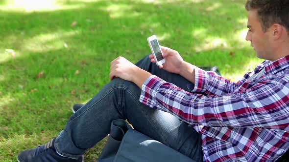 Handsome Young Student Sitting On The Grass Texting