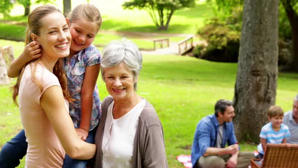 Three Generations Of Women Smiling At Camera With Men Behind