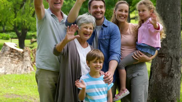 Multi Generation Family Posing And Waving At Camera In A Park