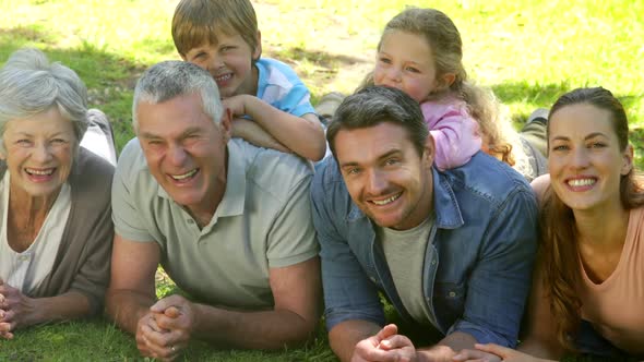 Multi Generation Family Smiling And Lying On Ground In A Park