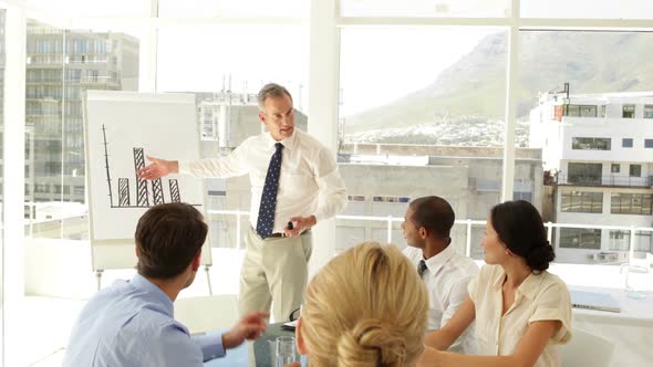 Businessman Explaining Bar Chart To His Staff At Presentation