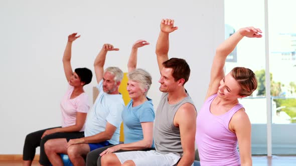 Fitness Group Sitting On Exercise Balls Stretching Arms alt