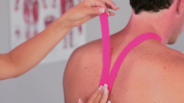 Physiotherapist Applying Pink Kinesio Tape To Male Patients Back