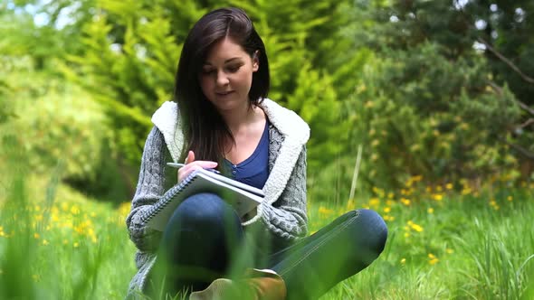Woman Sitting On Grass Writing On A Notebook