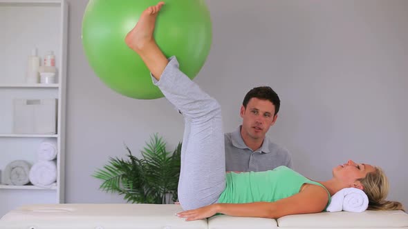 Physiotherapist Watching His Patient Move An Exercise Ball In Between Her Knees