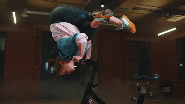 Athletic Girl Make Acrobatic Trick on Bike Exercising Workout on Stationary Cycling Machine Indoors