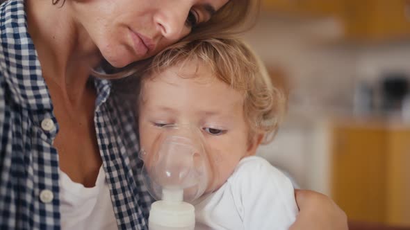 Baby Boy Breathes Through an Inhaler or Nebulizer While Sitting in His Mother's Arms