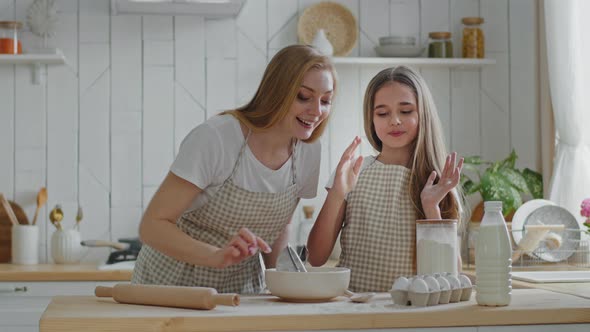 Adult Mother with Long Hair and Daughter Child Girl Cooking Dough Together at Home in Kitchen