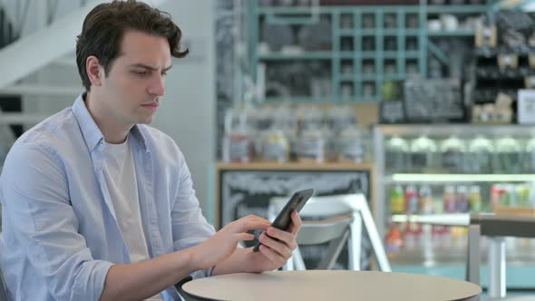 Attractive Young Man Using Smartphone in Cafe