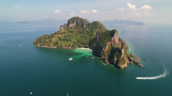 aerial drone circling around Ko Kai Island on a sunny summer day as a boat motors around the island