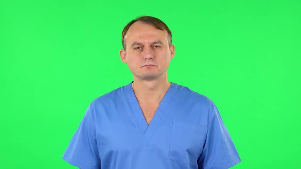 Medical Man Carefully Looks at the Camera in Frustration. Green Screen