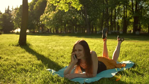 Pretty Girl Lying Down on a Meadow and Talking By Smartphone