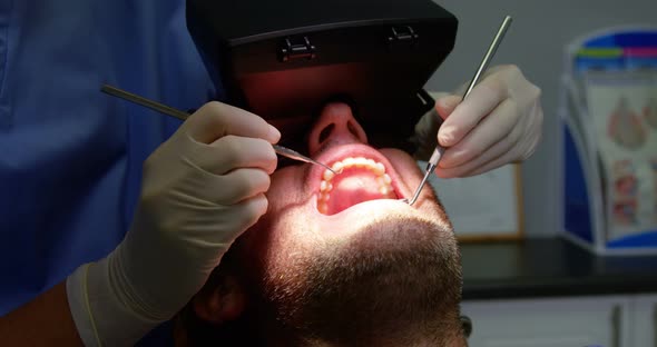 Dentist examining a male patient with dental tools