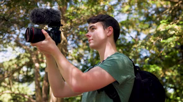 Close up of young male vlogger holding a professional camera shooting videos in a bright sunny fores