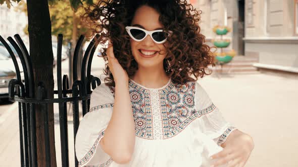 Beautiful smiling model with afro curls hairstyle dressed in summer hipster white dress