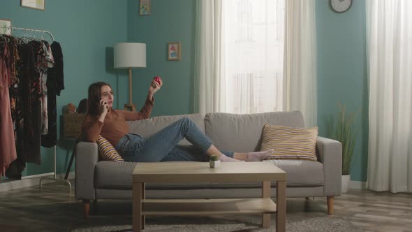 Woman with Red Apple Lies on Sofa and Talks on Phone