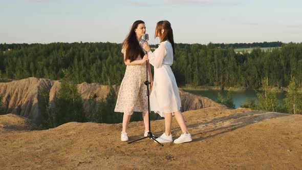 Two Attractive Women in White Dresses Sing Into Retro Shiny Microphone