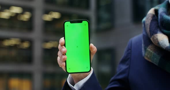 A Warmly Dressed Man Holds a Green Screen Phone
