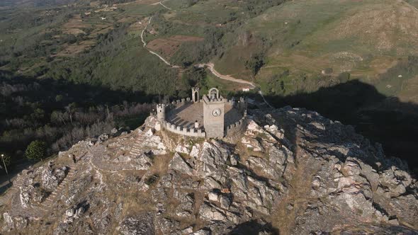 Tourist stands on the towers of the Folgosinho Castle as a drone circle at sunset.