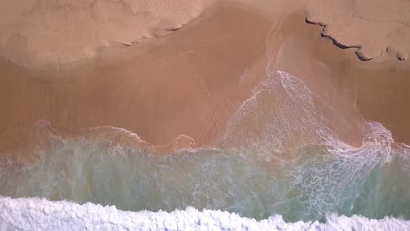 Top aerial view of tropical beach with turquoise ocean water and sea waves reaching shore.