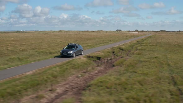 Slide and Pan Shot of Car Driving on Narrow Asphalt Path in Flat Landscape